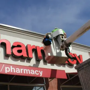 Main on a bucket truck installing red sign for pharmacy in daylight